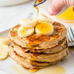 Pouring maple syrup over a stack of banana pancakes.