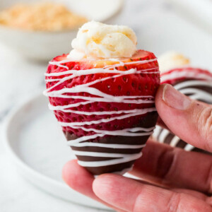 A hand holding a strawberry stuffed with cheesecake filling and dipped in chocolate.
