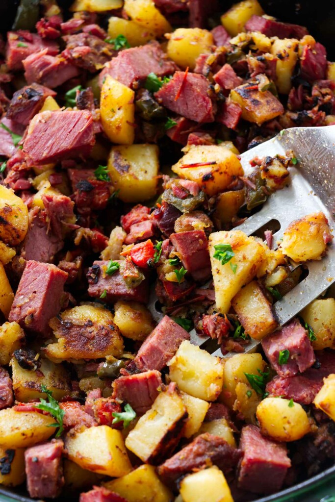 A corned beef hash recipe in a skillet with a spatula.