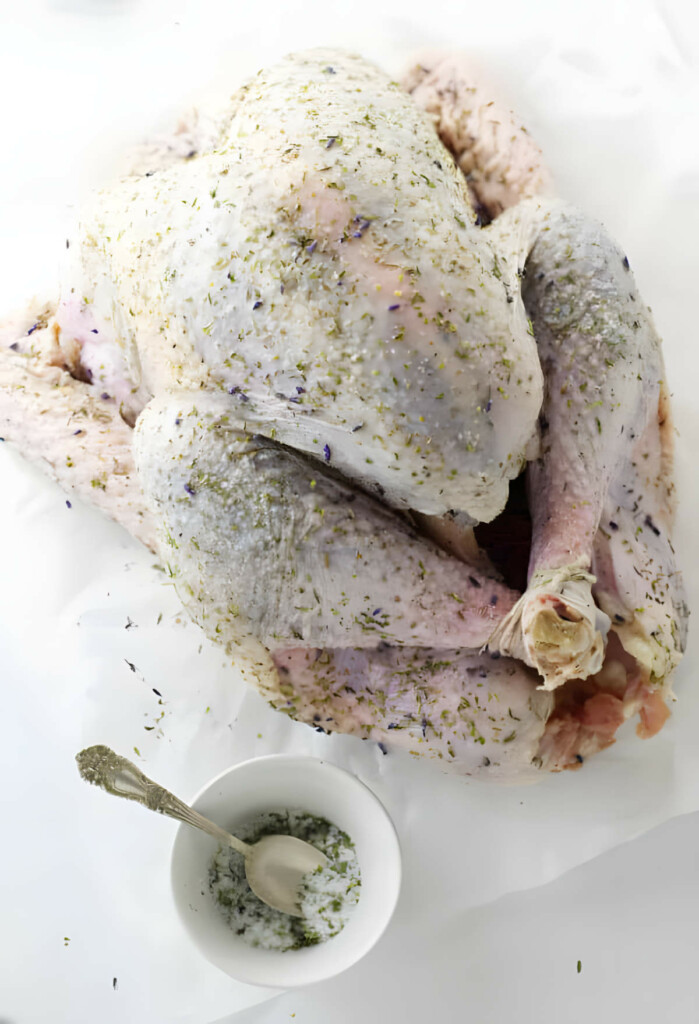 Coating a raw turkey in dry brine made with salt and herbs.