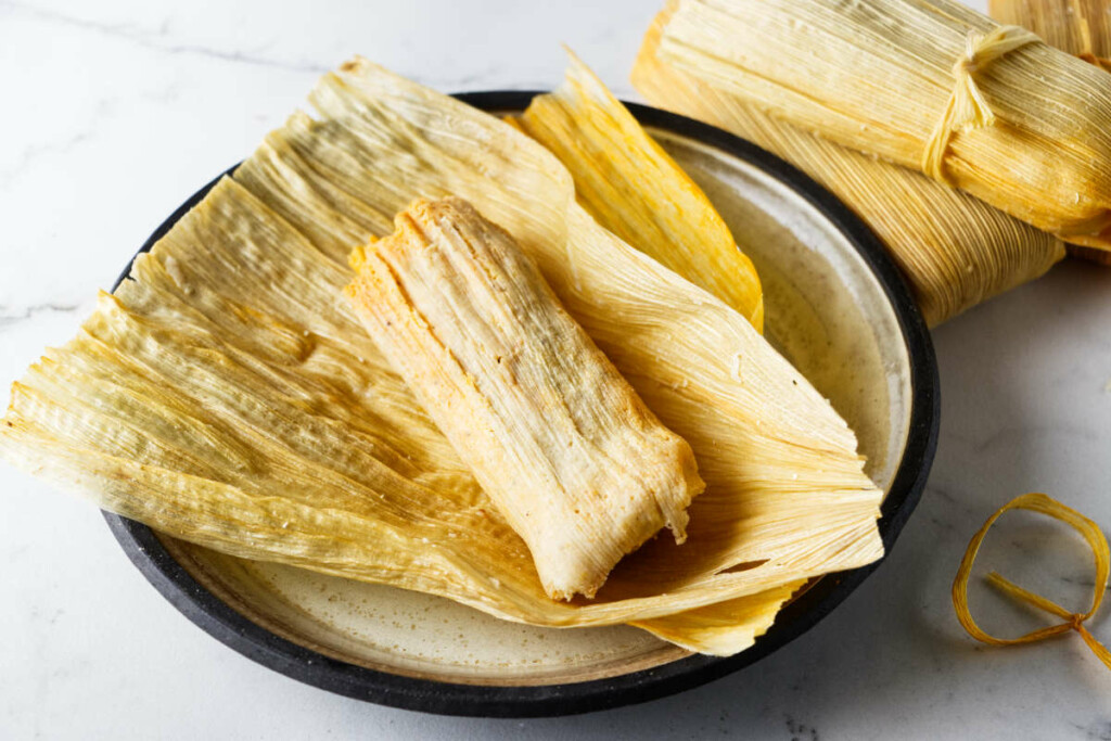 A tamale with the husk unwrapped and placed on a plate.