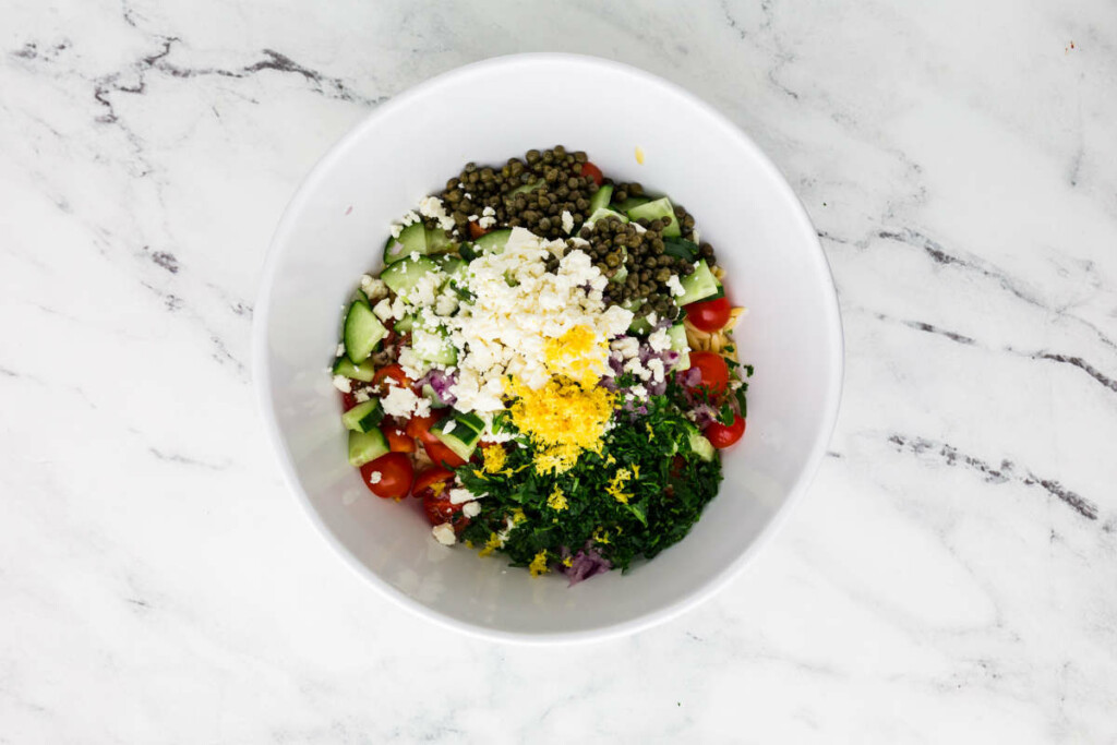 Tossing ingredients in a bowl for orzo salad with feta.