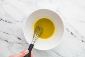 Whisking a lemon dijon dressing in a bowl.