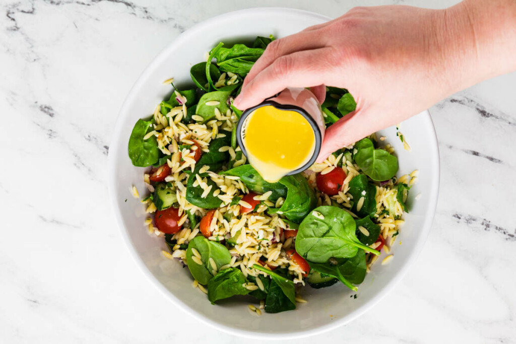 Adding dressing to lemon orzo salad recipe.