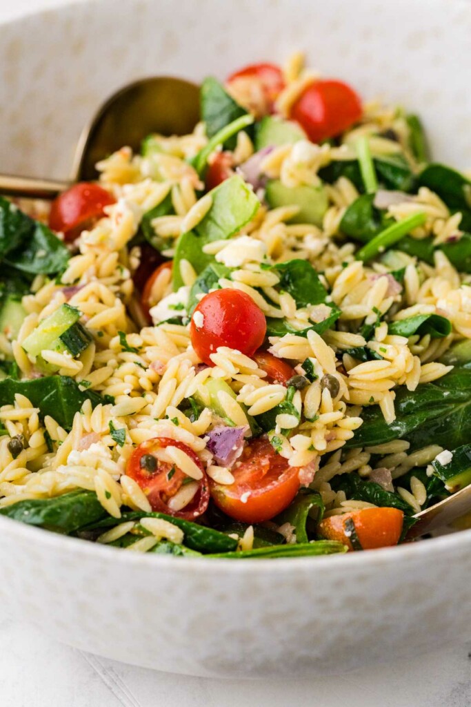 A lemon orzo salad in a bowl mixed with tomatoes, feta, and spinach.