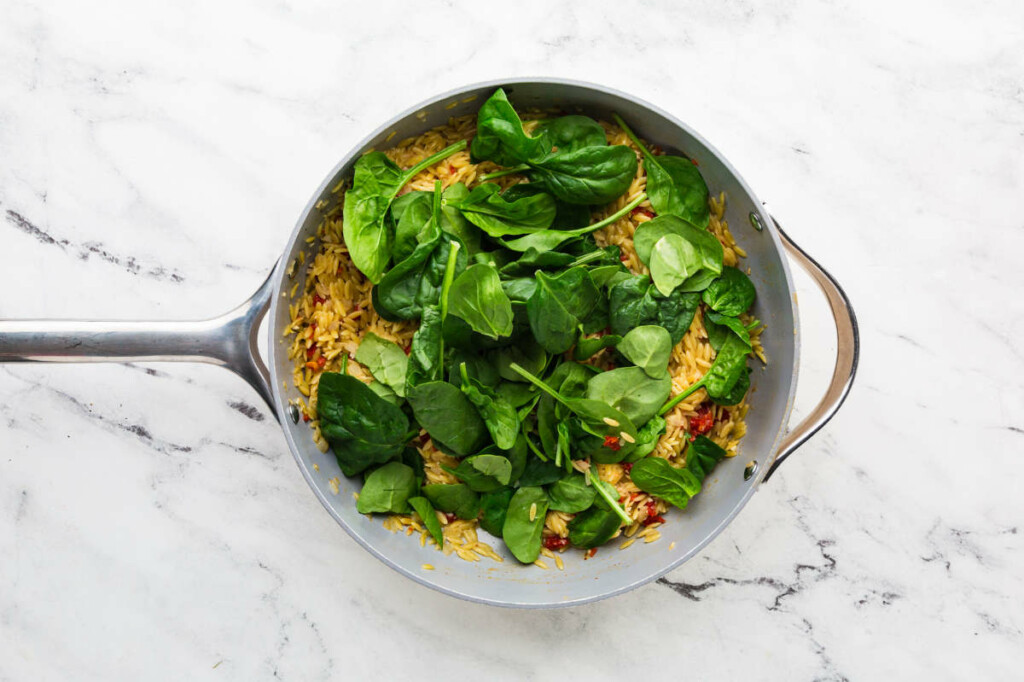 Adding fresh spinach to salmon and orzo skillet.