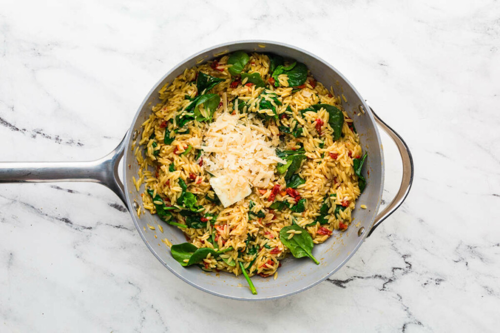 Adding cheese to a one pan salmon orzo.