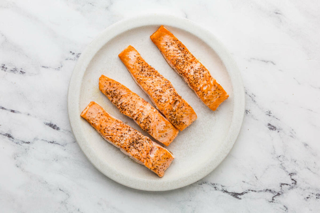 Setting salmon aside on a white plate.