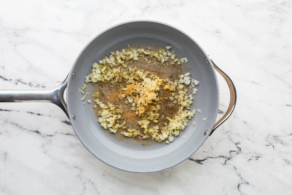 Cooking onions and garlic in a skillet prior to adding orzo and salmon.