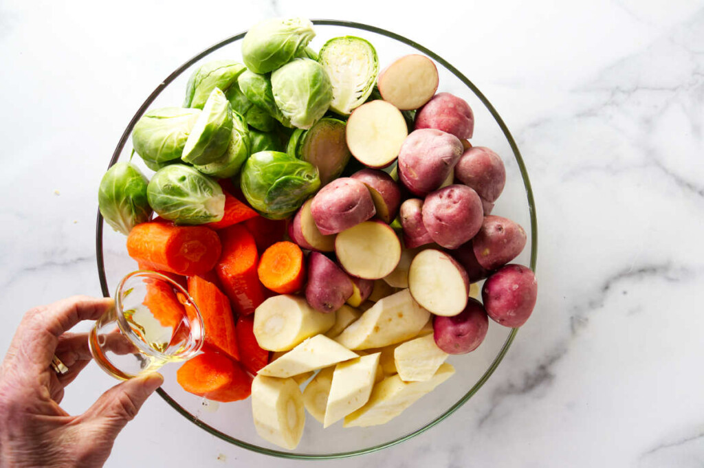 Tossing brussels sprouts, potatoes, carrots, and parsnips in a bowl with seasoning.