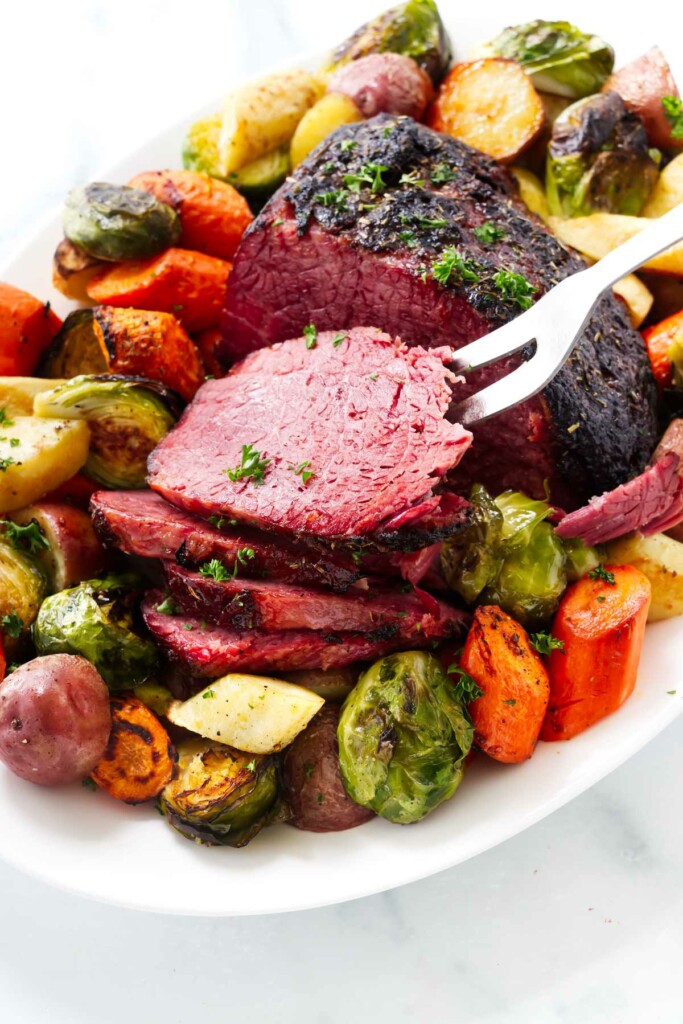 Slices of baked corned beef on a plate with vegetables.