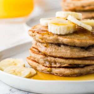 A stack of sourdough discard banana pancakes with a glass of orange juice.