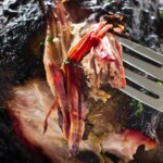 Close-up of fork shredding juicy, smoky barbeque with herbs garnish.