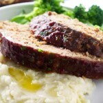 Glazed meatloaf with potatoes and broccoli on a white plate.