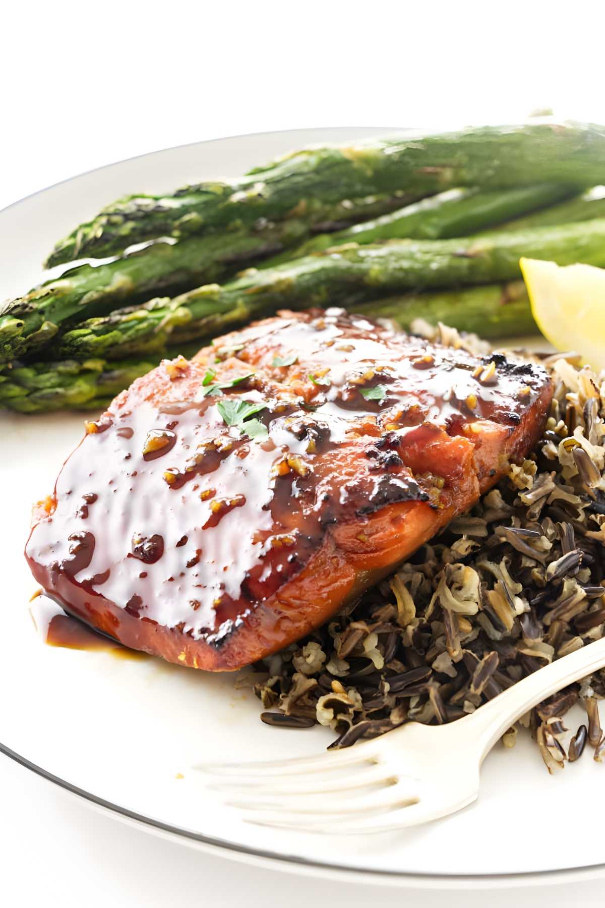 Grilled salmon with wild rice, roasted asparagus, and lemon wedge on plate.