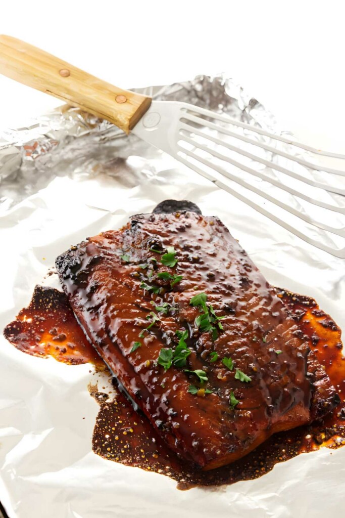 Glazed salmon on foil, garnished with herbs, beside a spatula.