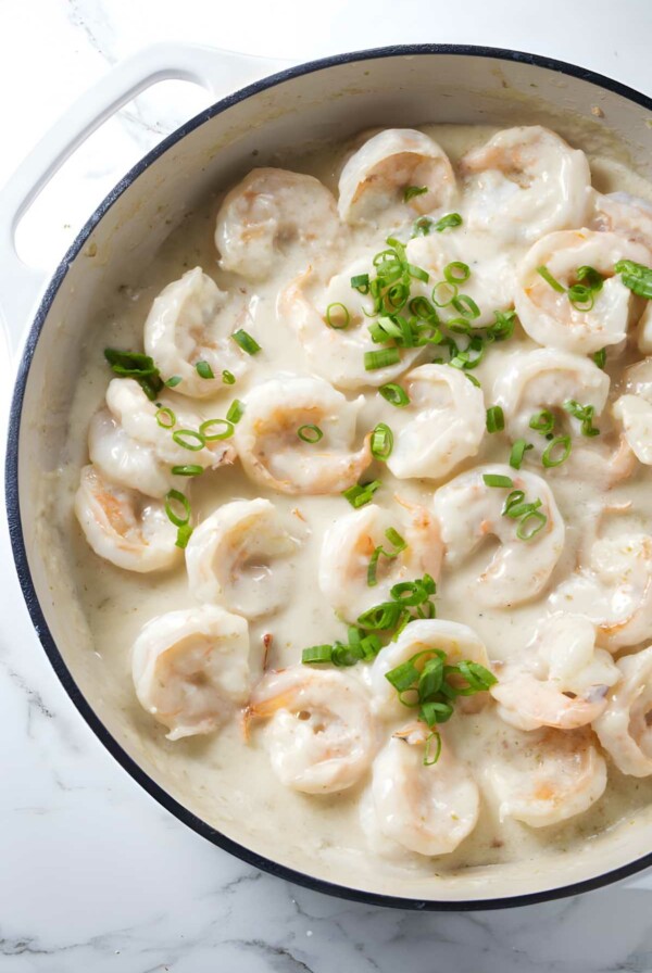 Shrimp in creamy white sauce with green onions in skillet on marble.