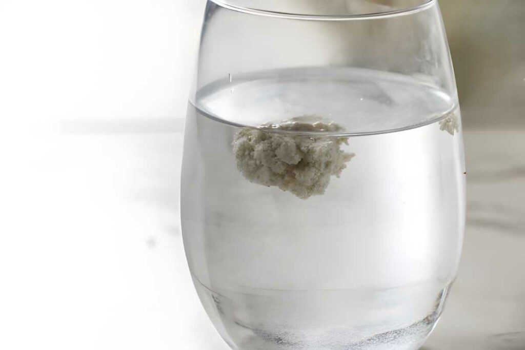 Clear glass of water with baking soda floating, plain softly lit background.