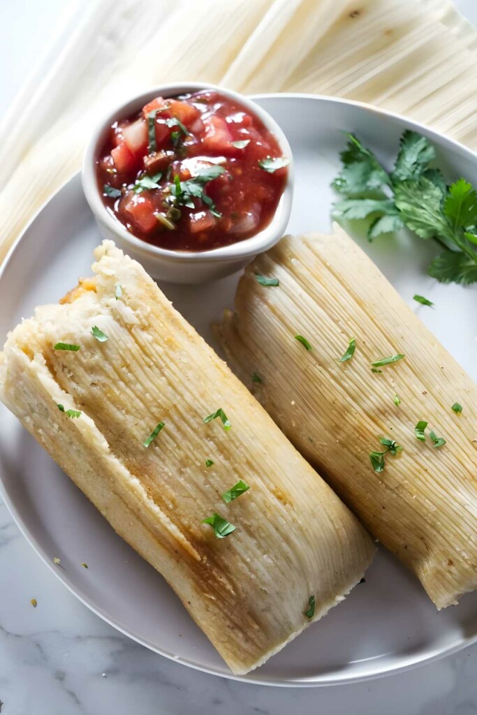 Two tamales on plate with salsa and fresh cilantro garnish.