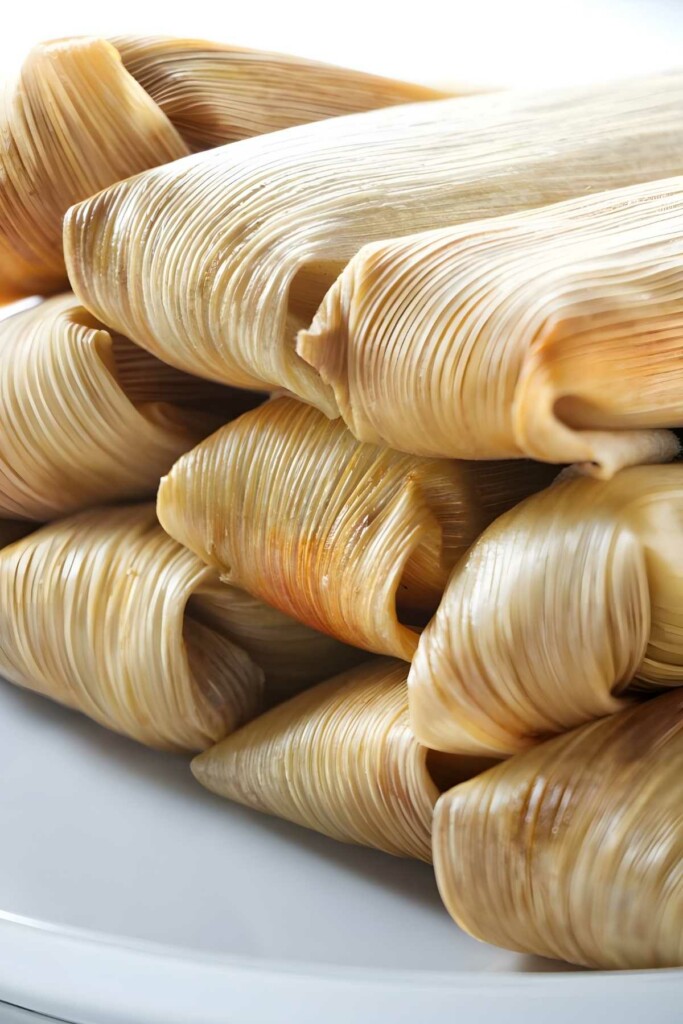 Close-up of golden-brown tamales wrapped in corn husks on plate.