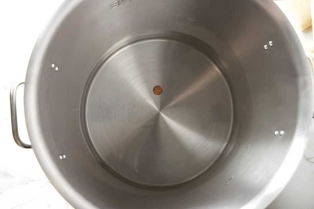 Large empty stainless steel pot with brown spot, viewed from above.