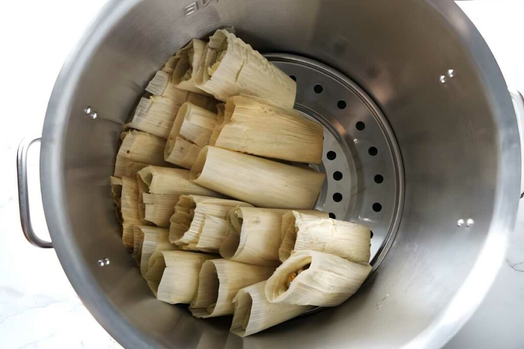Large steamer pot filled with upright, corn husk-wrapped tamales.