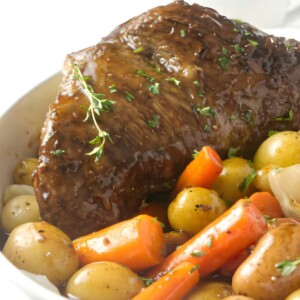 Glazed pot roast with potatoes, carrots, onions, thyme, and sauce.