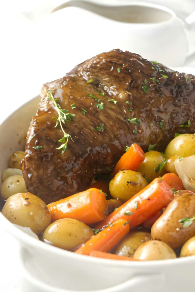 Glazed pot roast with potatoes, carrots, onions, thyme, and sauce.