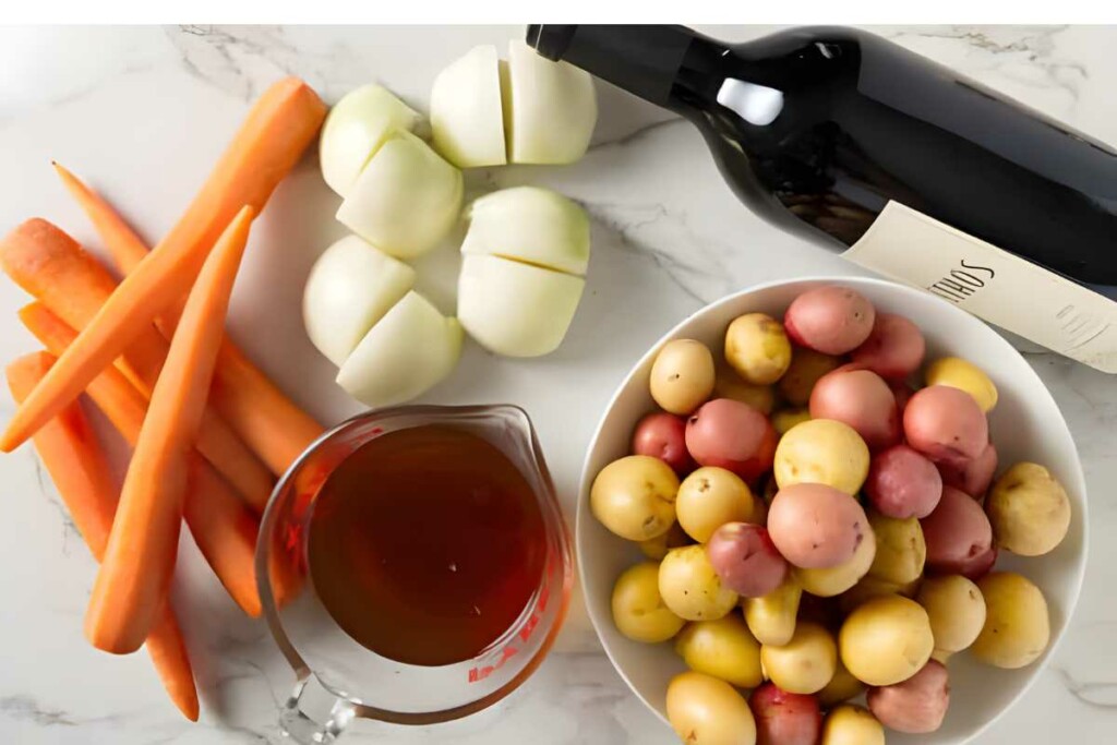 Ingredients on marble: carrots, onions, potatoes, broth, and red wine.
