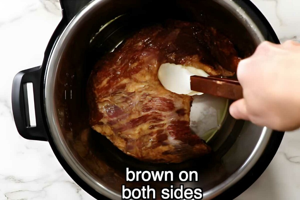 Hand browning meat with tongs in Instant Pot, text: brown on both sides.
