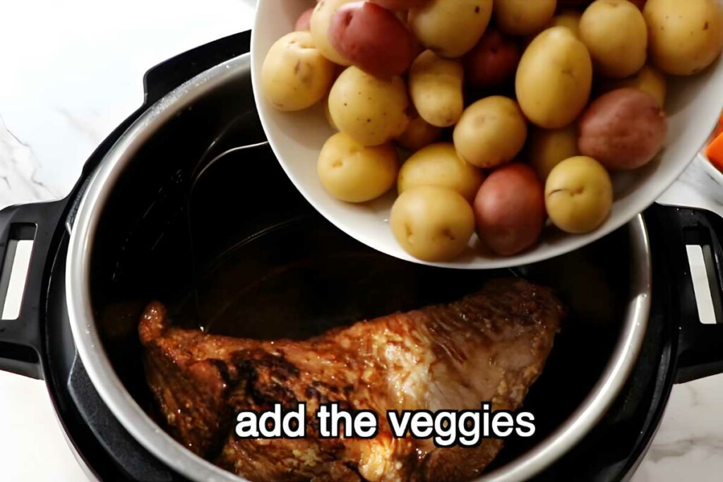Bowl of potatoes added to pressure cooker with cooked meat, add the veggies.