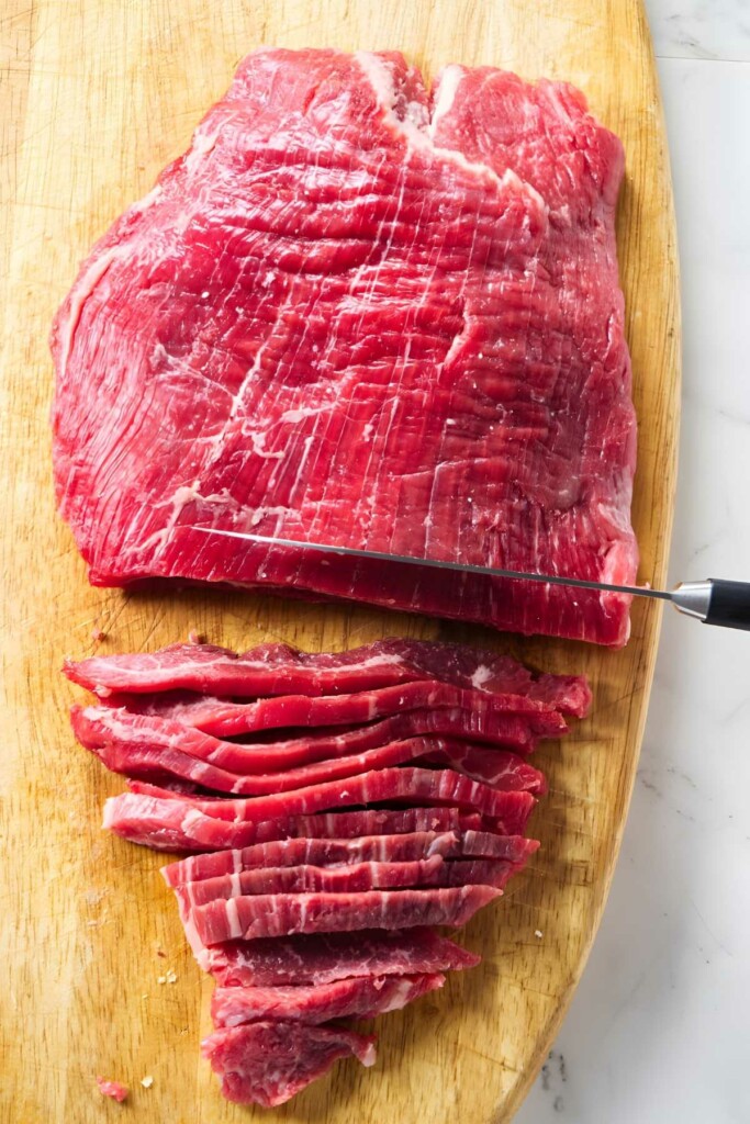 Raw flank steak partially sliced on a cutting board with visible knife.