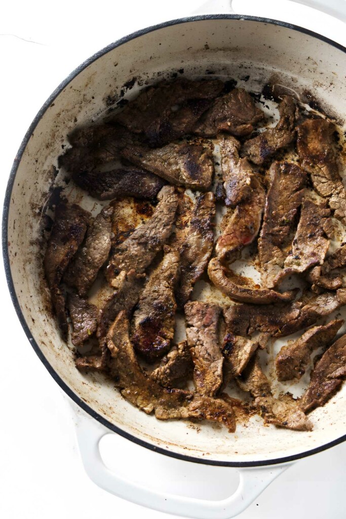Browned, sliced beef liver pieces in white cast iron skillet.