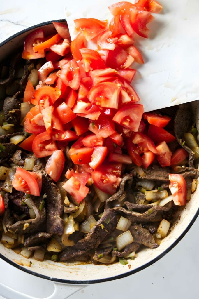 Sliced tomatoes added to pan with cooked beef strips and onions.