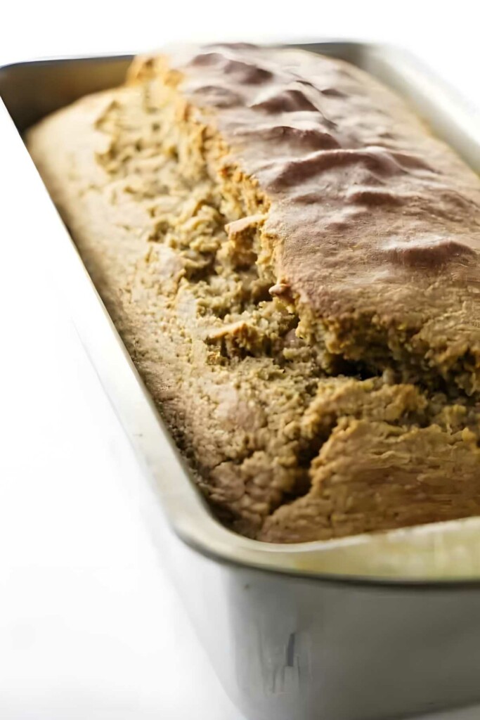 Close-up of golden-brown banana bread loaf in metal pan, cracked top.