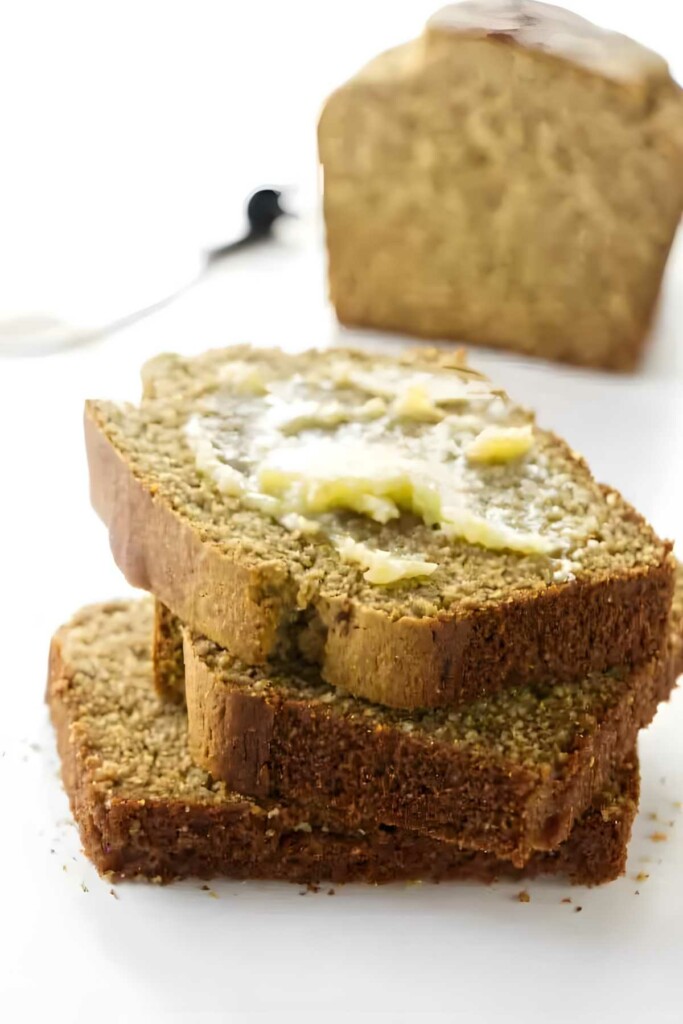 Three stacked bread slices with melting butter, loaf in background.