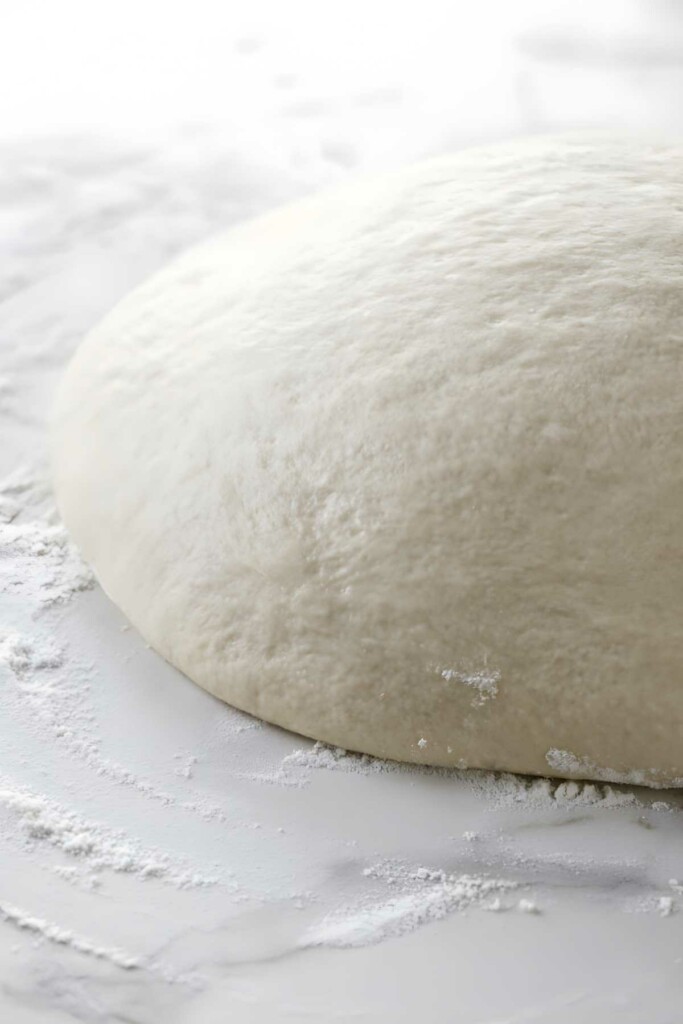 Close-up of risen pizza dough on a floured surface, smooth and airy.