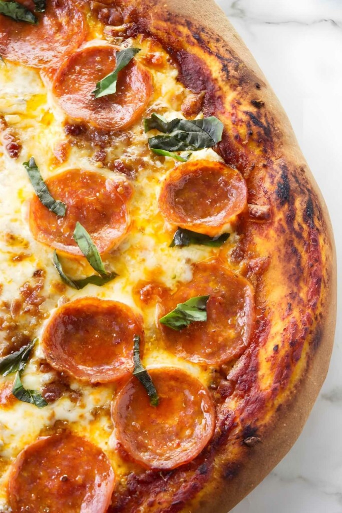Close-up of pepperoni pizza with melted cheese and basil on thick crust.