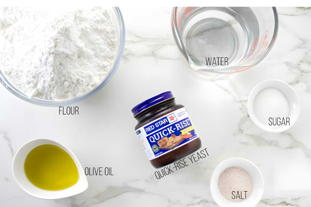 Bread dough ingredients arranged on a marble surface: flour, water, yeast, seasonings.