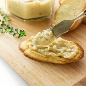 Knife spreading roasted garlic on toast.