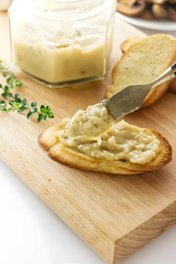 Knife spreading roasted garlic on toast.