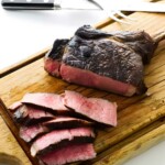 Sliced medium-rare steak on board with carving fork and knife.