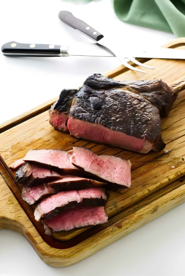 Sliced medium-rare steak on board with carving fork and knife.