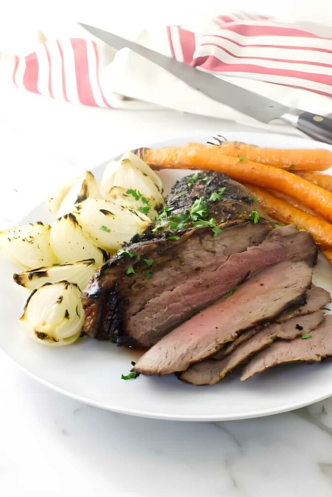 Sliced roast beef with onions and carrots on a white plate.