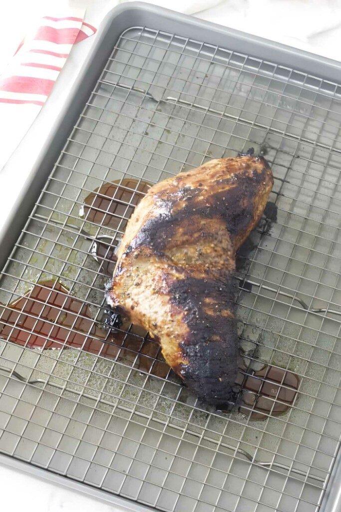 Partially burnt chicken on wire rack above tray, striped cloth nearby.