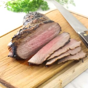 Sliced tri tip on cutting board with knife and parsley in background.