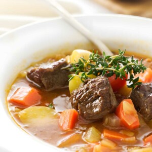 Close-up of lamb soup with vegetables, bread in background.
