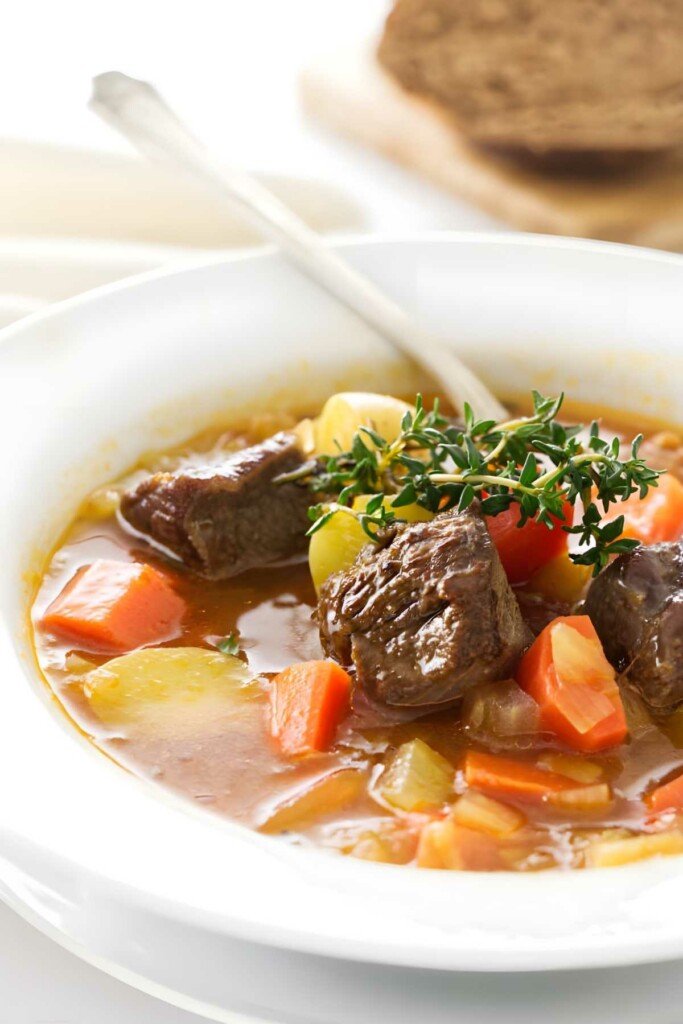 Close-up of lamb soup with vegetables, bread in background.