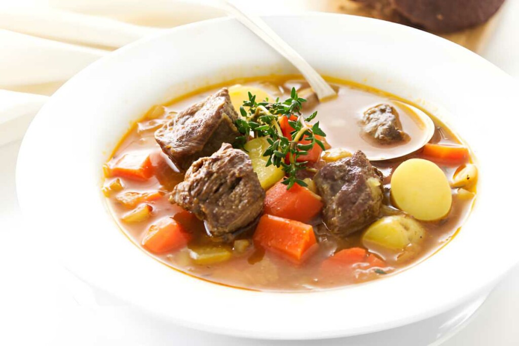 Bowl of lamb soup with vegetables and herbs.