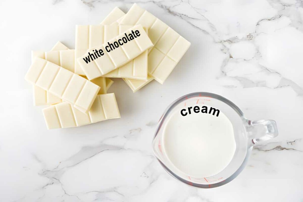 White chocolate bars and measuring cup of cream on marble surface.